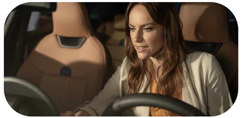 A woman looks down at the MINI OLED Display from the driver's seat of her MINI.