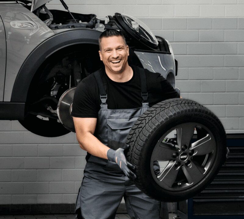 service-center-hero.png A man lifting a tire servicing a car