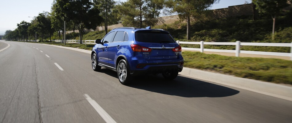 A blue Mitsubishi Outlander driving down an open road A Mitsubishi Outlander Sport driving long a white fence