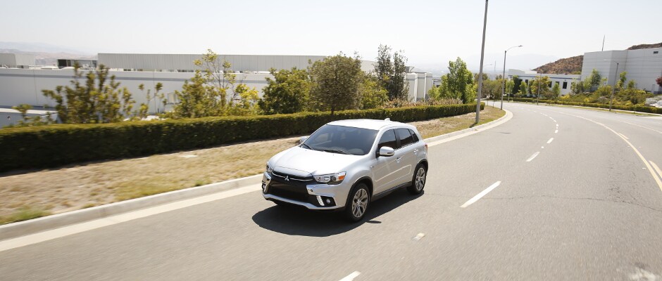 A white Mitsubishi Outlander driving down the road A white Mitsubishi Outlander Sport driving down a road on a nice day