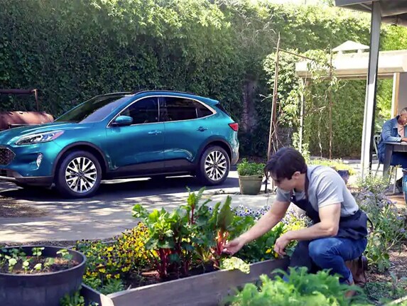 A man and woman working in their yard with a 2020 Ford Escape parked in the background