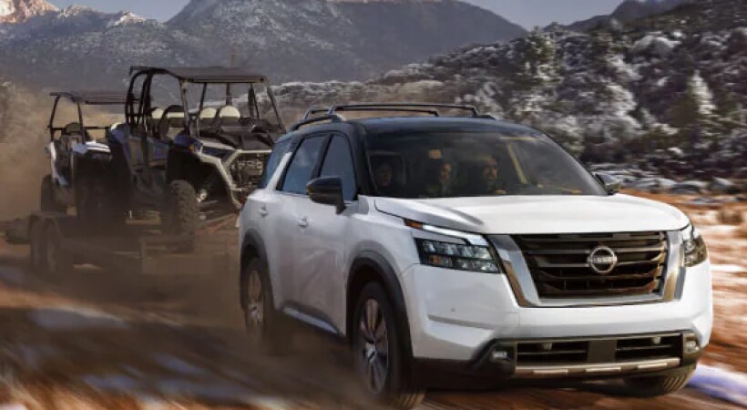 White Nissan SUV towing 2 ATV's
