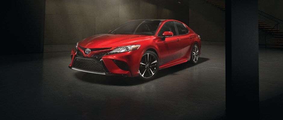 2018 Toyota Camry Packages A red 2018 Toyota Camry parked in a warehouse