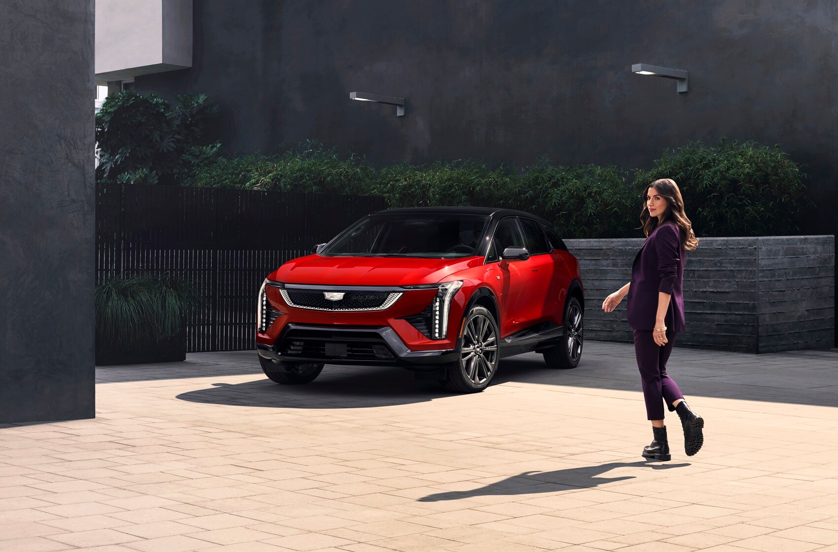 Woman walking to parked Cadillac OPTIQ while looking over shoulder at camera