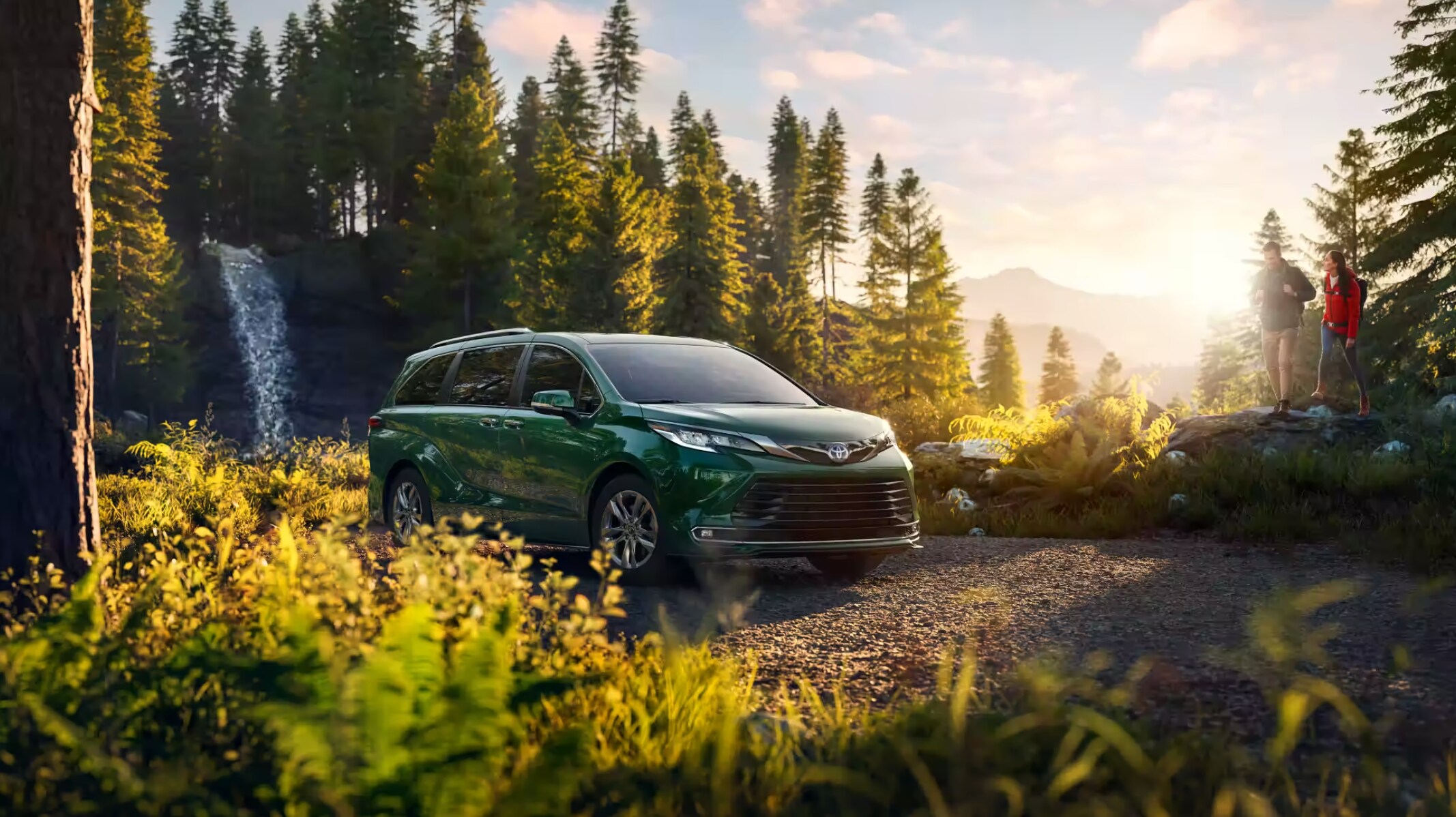 Toyota Camry vs. Honda Odyssey Green 2023 Toyota Sienna parked at a camp site with trees in background and couple in frame
