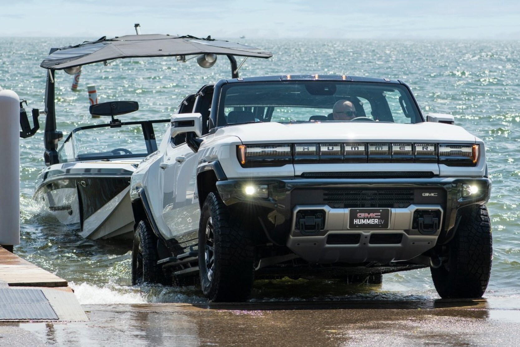 2024 GMC Hummer EV Pickup Truck towing a larger boat out of the water at a dock ramp