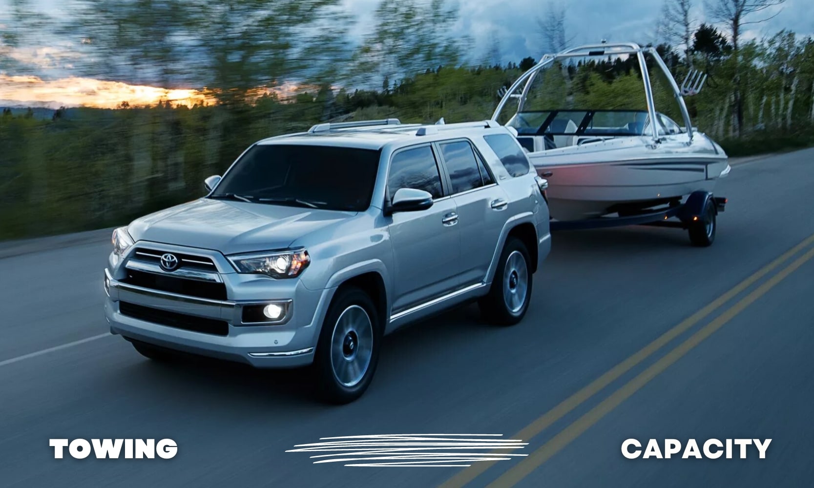 a silver used Toyota 4Runner SUV towing a large boat down an open country road