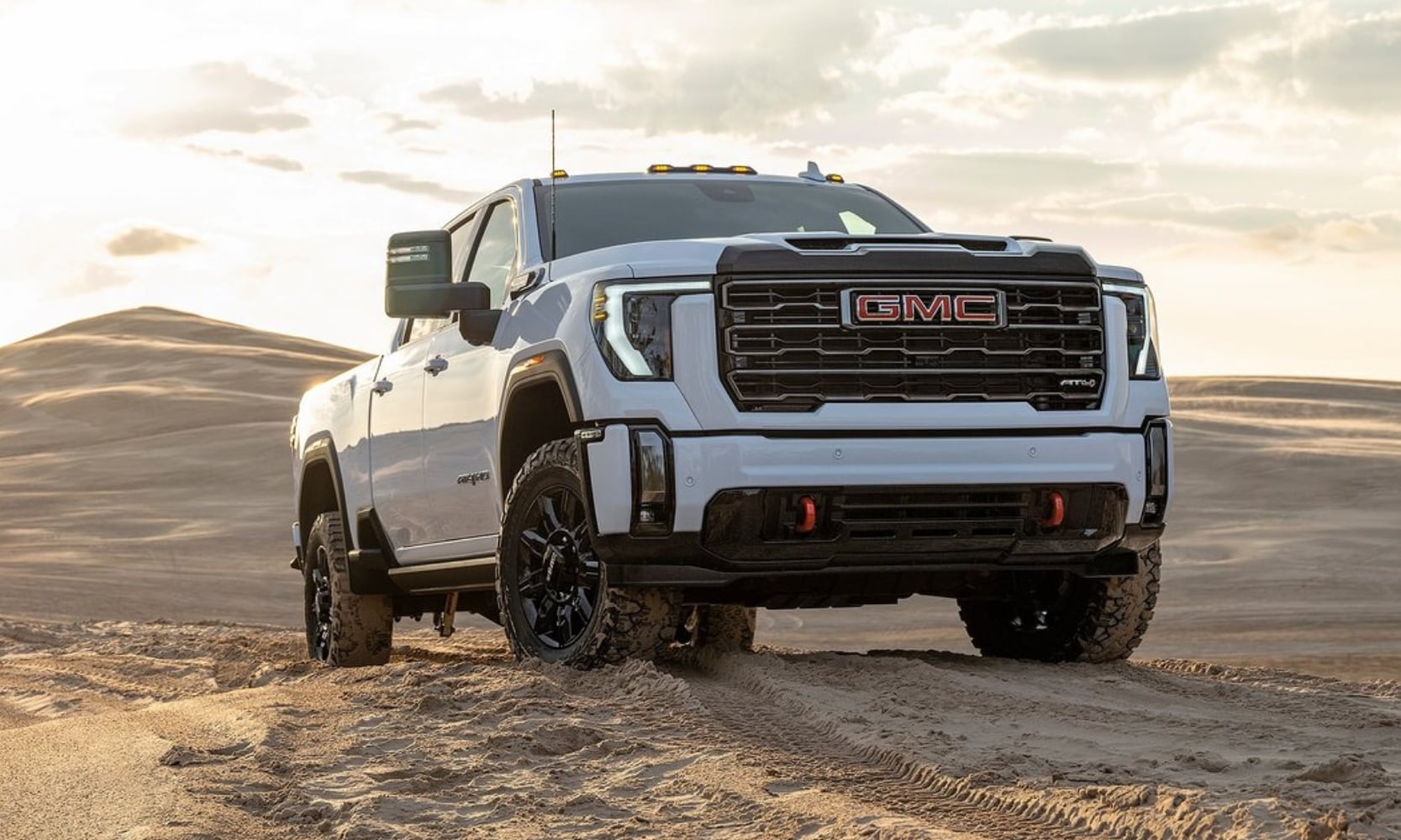Powerful front profile view of a white 2024 GMC Sierra 2500 HD AT4 off-road truck parked on top of a sandy dune