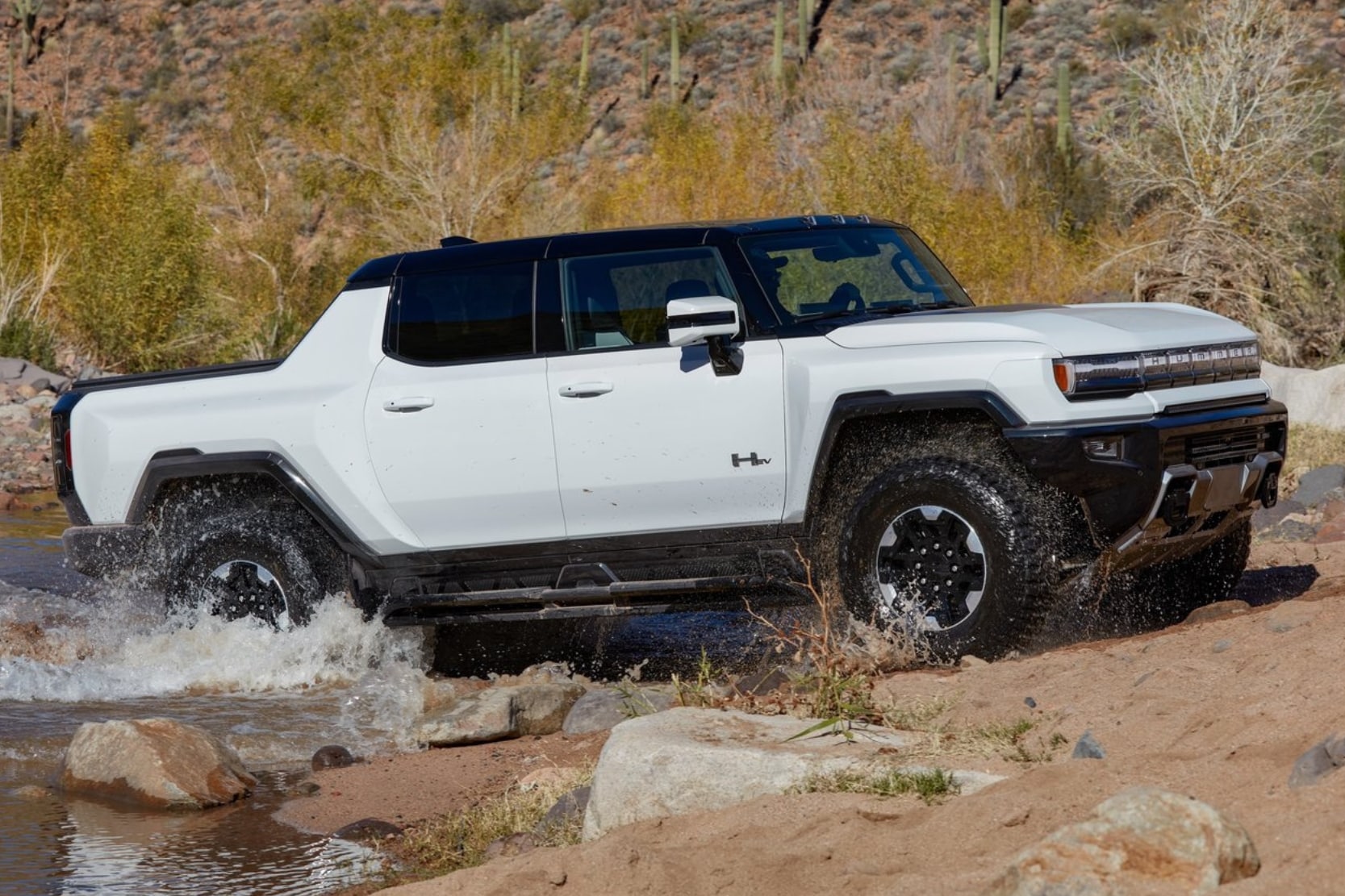 a white 2024 GMC Hummer EV Pickup Truck pulling out of a river bank with ease on an off-road desert trail