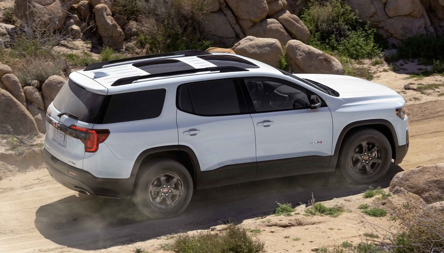 Aerial view of a 2023 GMC Acadia AT4 SUV driving down an off-road trail in the desert