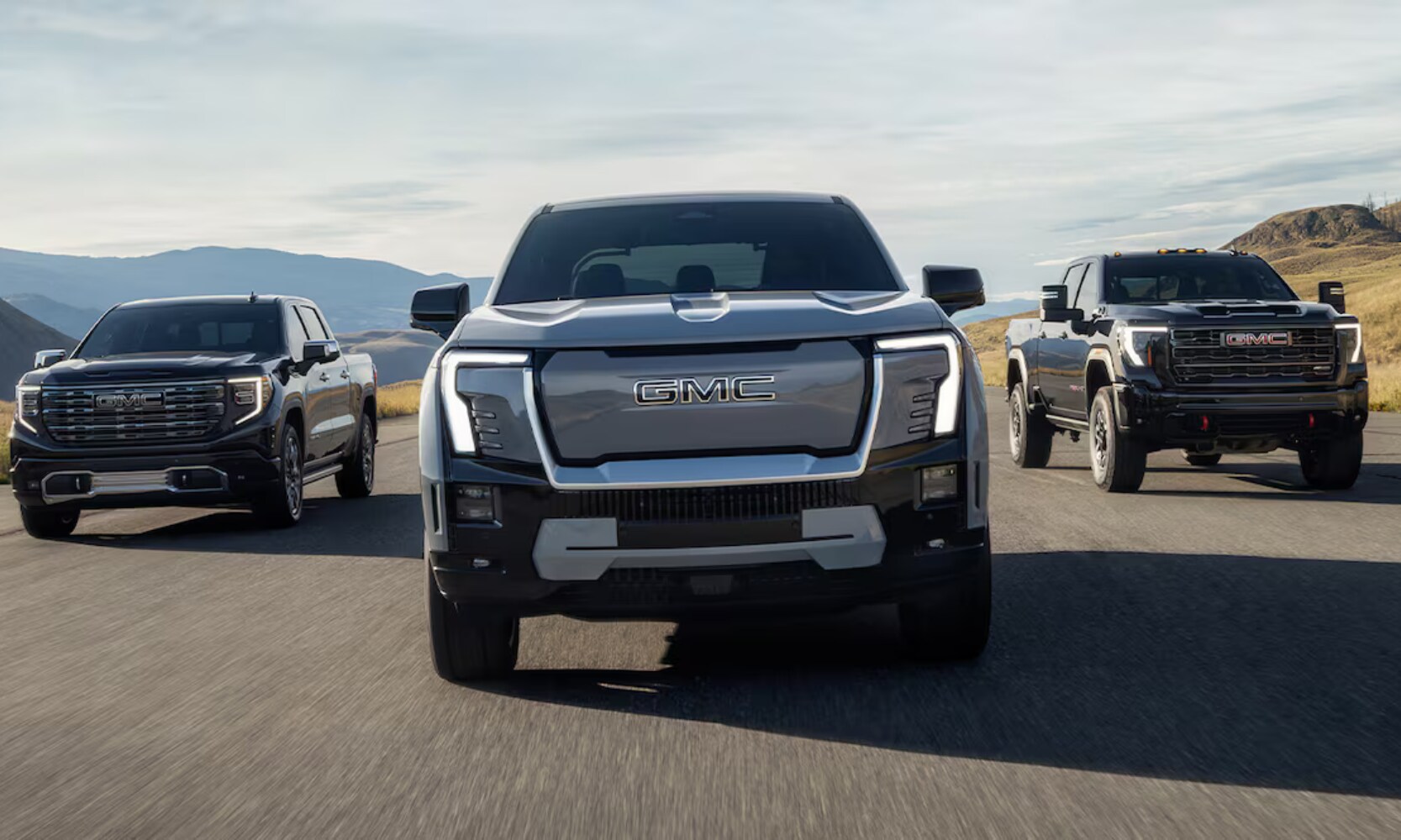 2026%20GMC%20Sierra%20EV%20Trim%20Levels%20-%20Octane%20GMC%20of%20Santa%20Fe.png Exterior front image of the 2026 GMC Sierra EV Elevation, AT4, and Denali trims driving down a mountainous freeway