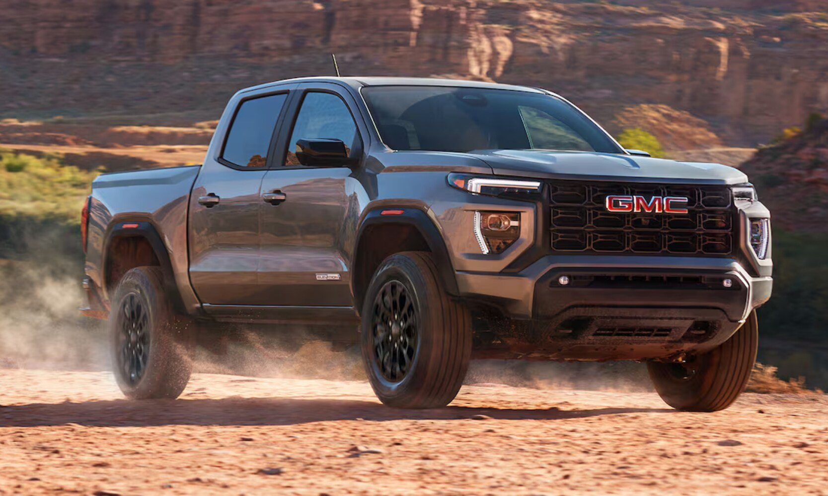 2026%20GMC%20Canyon%20Elevation%20-%20Octane%20GMC%20of%20Santa%20Fe.png Exterior side angle image of a gray 2026 GMC Canyon Elevation driving through dirt in a rocky mountainous landscape