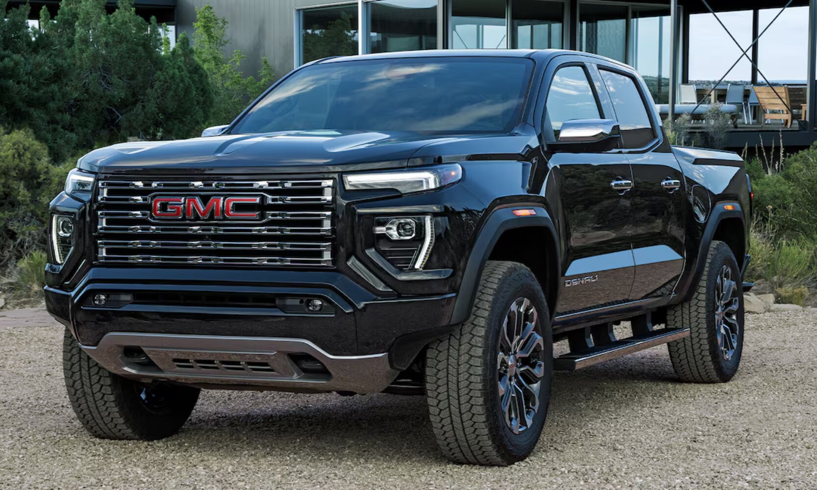 2026%20GMC%20Canyon%20Denali%20-%20Octane%20GMC%20of%20Santa%20Fe.png Exterior front angle image of a black 2026 GMC Canyon parked in a modern home's rocky driveway