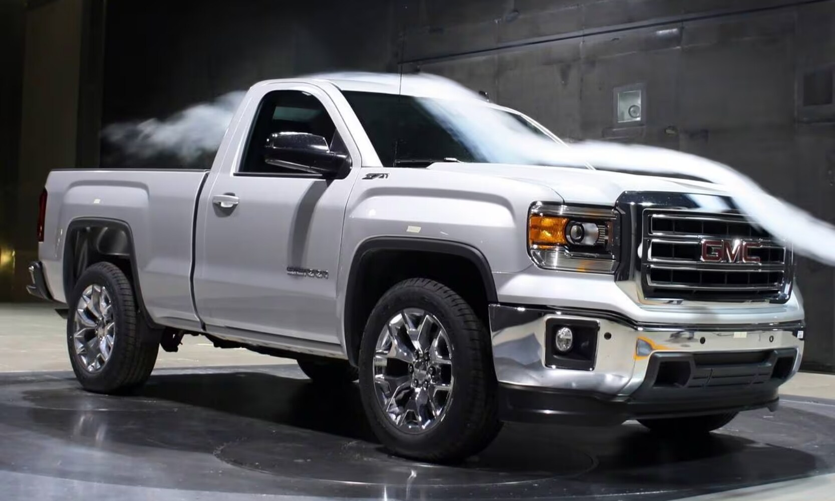 photo of a white 2014 GMC Sierra 2500 HD SLE Truck inside a GMC showroom with a fog machine blowing