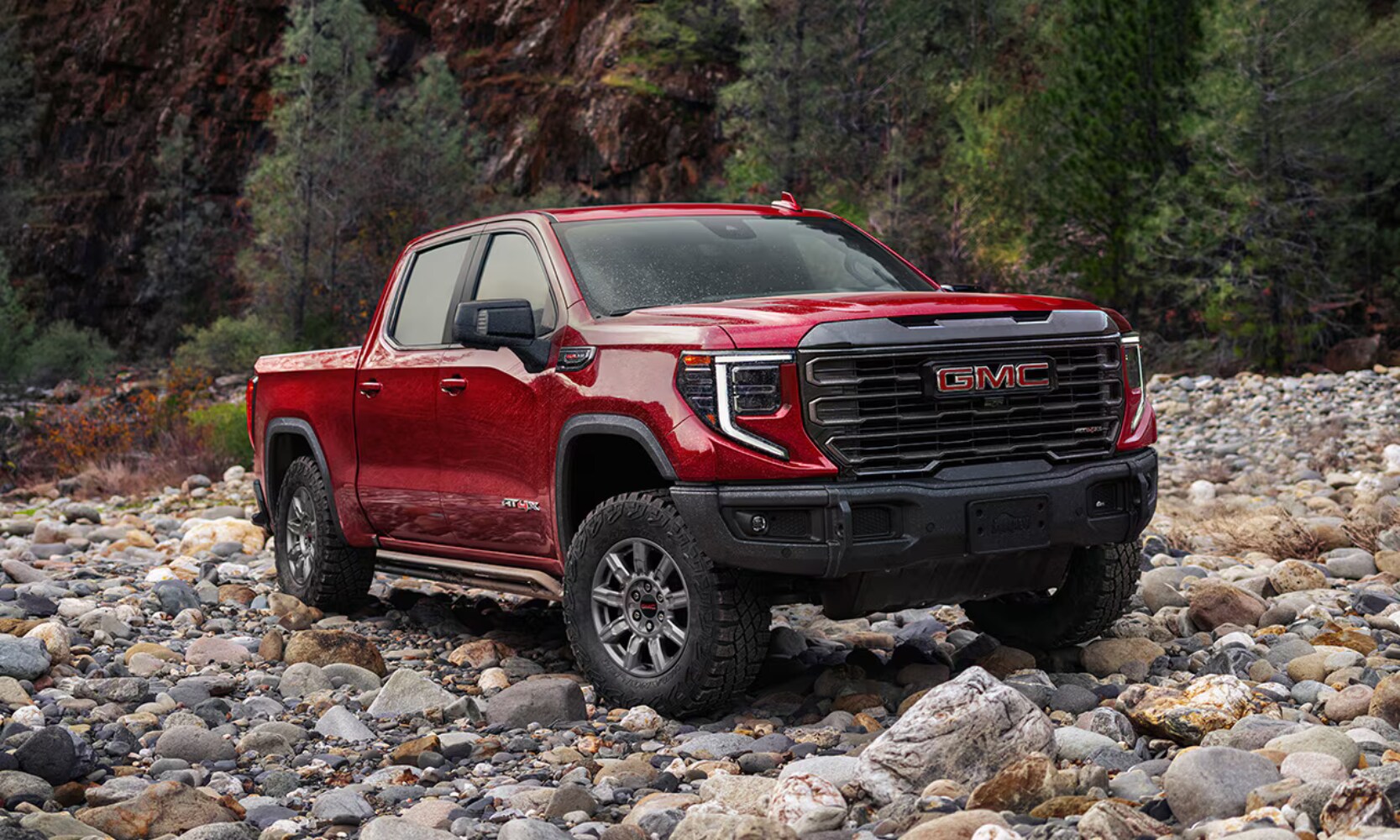 2026%20GMC%20Sierra%201500%20AT4X%20-%20Octane%20GMC%20of%20Santa%20Fe.png Exterior front side angle image of a red 2026 GMC Sierra 1500 AT4X parked on rocky terrain in a forest