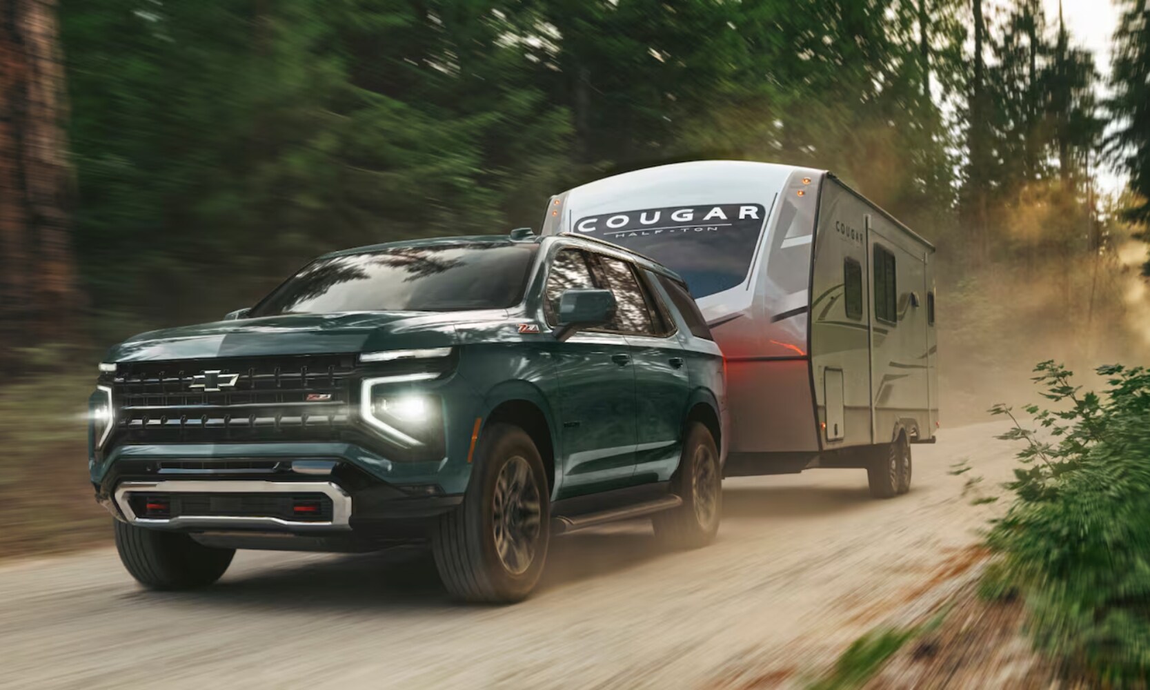 2025%20GMC%20Yukon%20vs.%202025%20Chevrolet%20Tahoe%20-%202025%20Chevy%20Tahoe%20Towing%20Comparison%20-%20Octane%20GMC%20of%20Santa%20Fe.jpg Exterior image of a teal 2025 Chevy Tahoe Z71 towing a camping trailer on a dirt road through a forest during the day