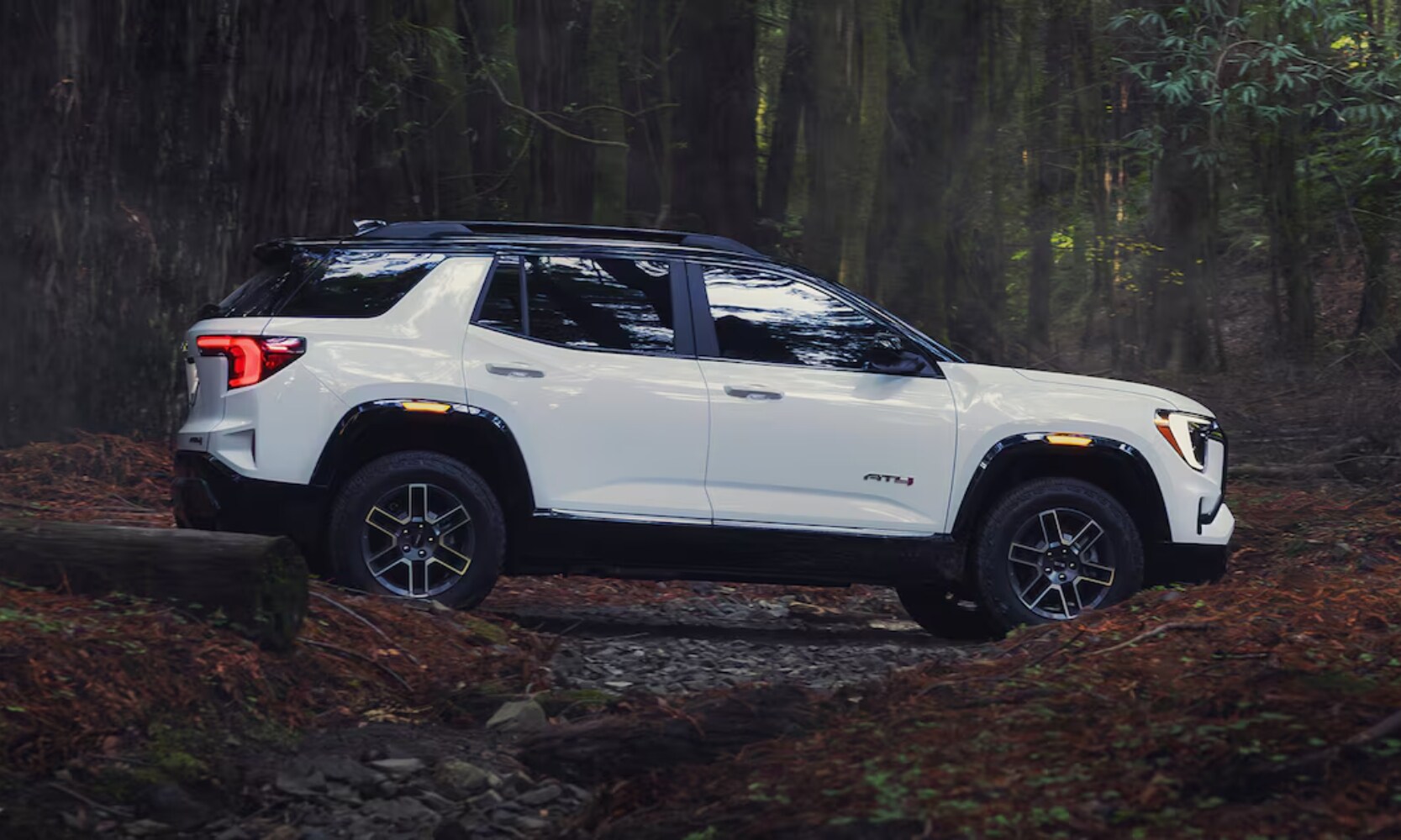 2026 GMC Terrain AT4 - Octane GMC of Santa Fe.jpg Exterior side image of a white 2026 GMC Terrain AT4 driving through the woods in an off-road area