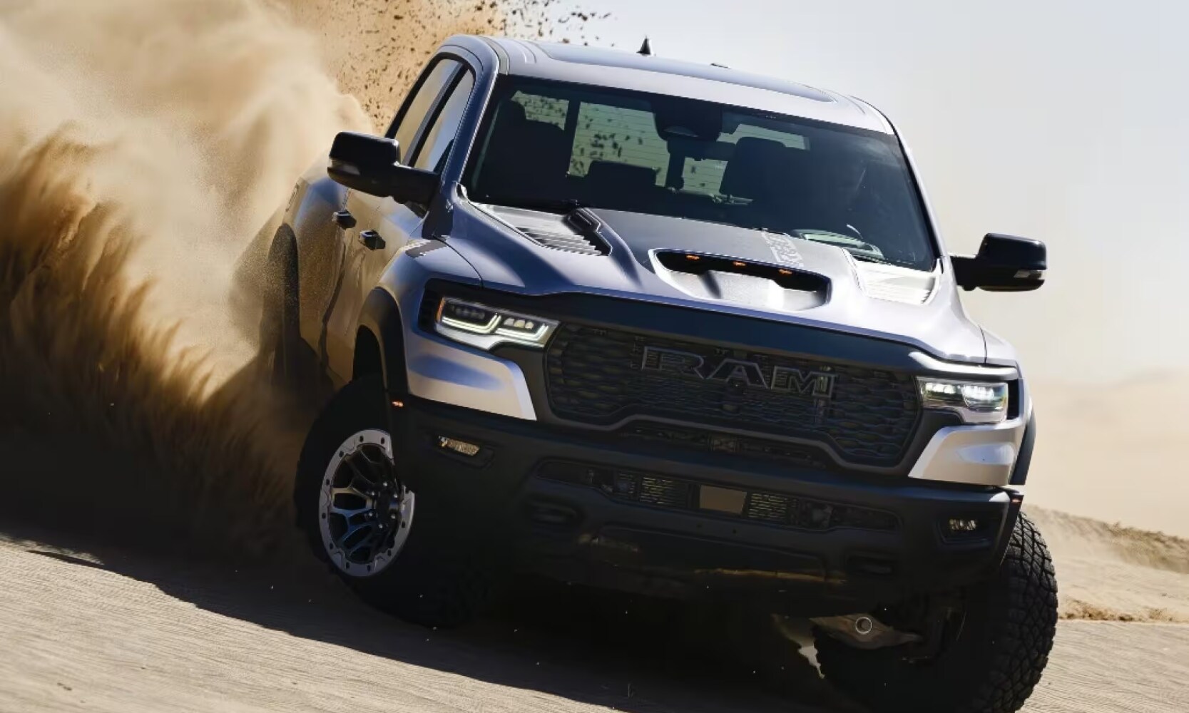 2025%20GMC%20Sierra%201500%20vs.%202025%20RAM%201500%20-%202025%20RAM%201500%20Off-Road%20Comparison%20-%20Octane%20GMC%20of%20Santa%20Fe.jpg Exterior front image of a silver 2025 RAM 1500 off-roading in a dirt landscape during the day