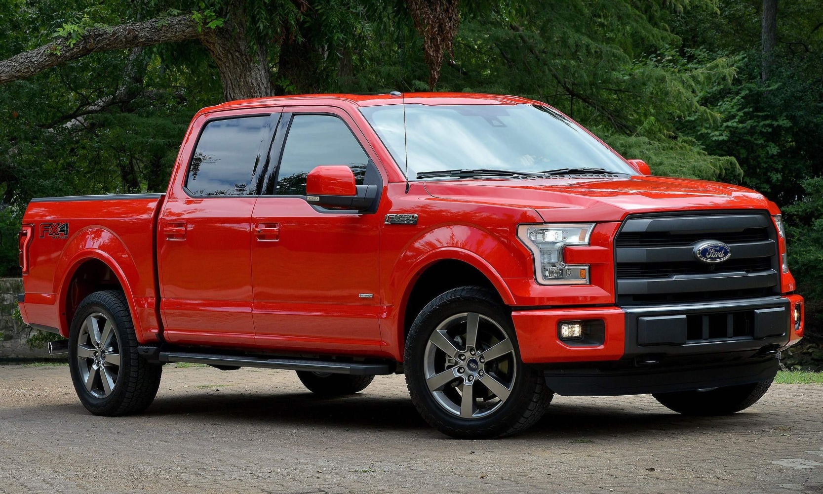 Best Trucks to Buy Used in 2026 - 2015 Ford F-150 Octane GMC.png Exterior image of a red 2015 Ford F-150 parked in a driveway in front of trees