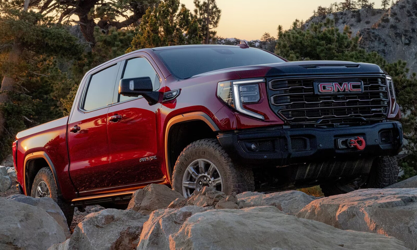 2025%20GMC%20Sierra%201500%20vs.%202025%20RAM%201500%20-%202025%20Sierra%201500%20AT4X%20-%20Octane%20GMC%20of%20Santa%20Fe.jpg Exterior front side angle image of a red 2025 GMC Sierra 1500 AT4X parked on a rocky incline during sunset