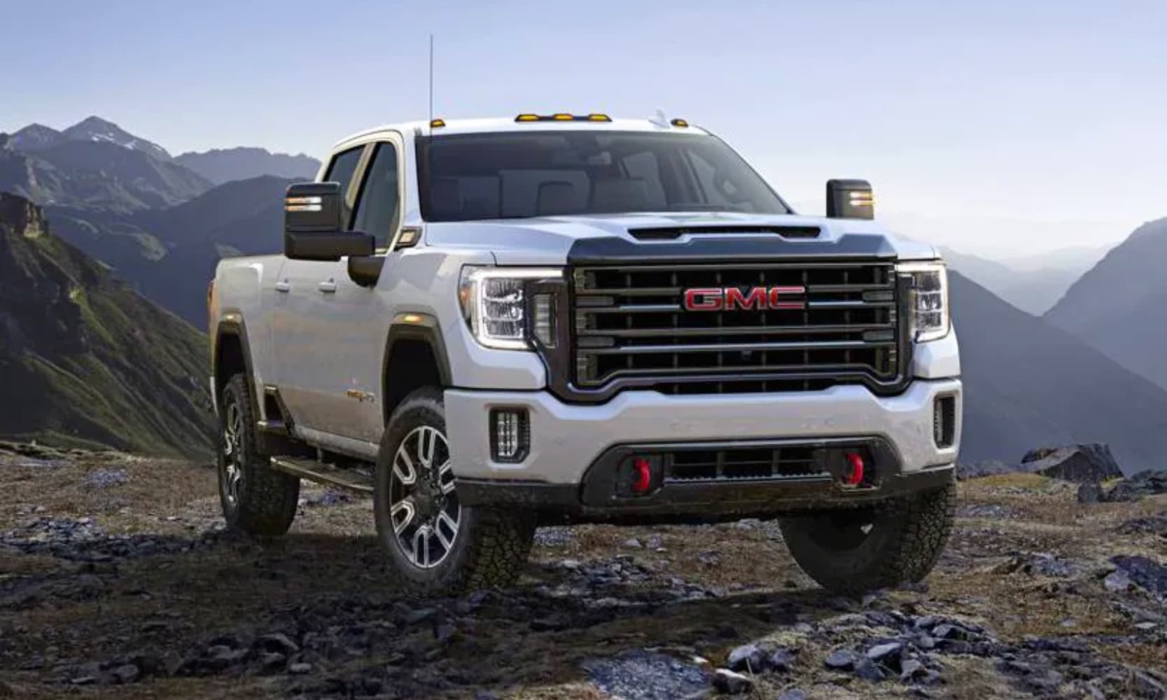 photo of a white 2020 GMC Sierra HD AT4 Crew Cab Truck on top of a mountain with mountains in the background