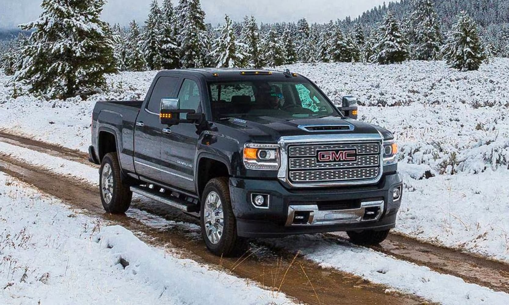 photo of a black 2016 GMC Sierra 2500 HD Denali Truck on a dirt and snowy road with pine trees in the background