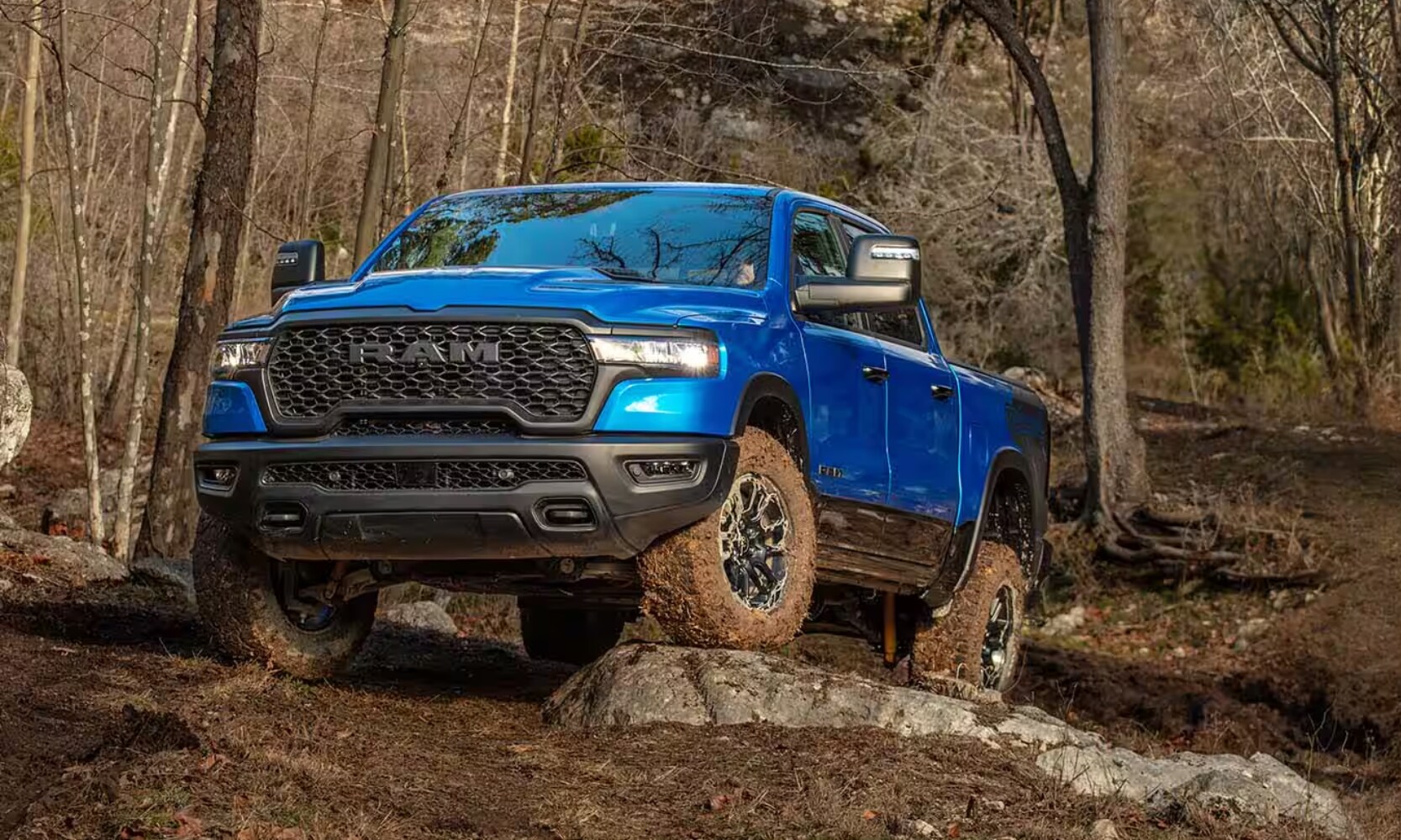 2025%20GMC%20Sierra%201500%20vs.%202025%20RAM%201500%20-%202025%20RAM%201500%20Rebel%20-%20Octane%20GMC%20of%20Santa%20Fe.jpg Exterior image of a blue 2025 RAM 1500 Rebel parked on a rocky dirt incline in a forest setting