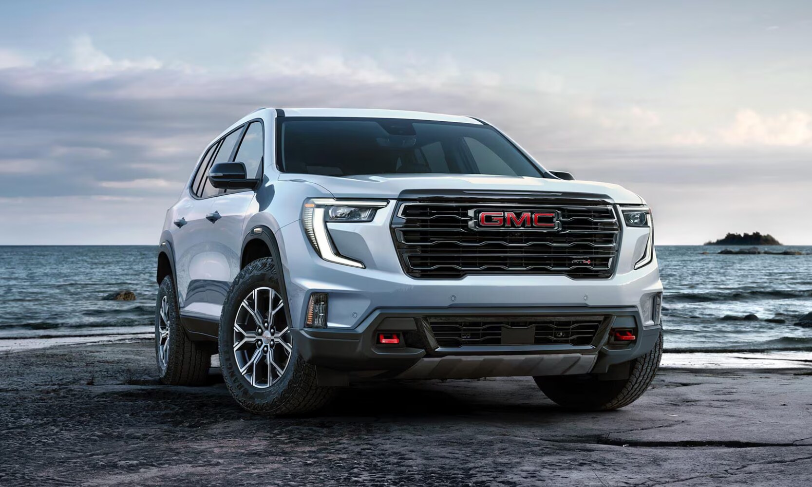2026 GMC Acadia AT4 Octane GMC of Santa Fe.png Exterior front image of a white 2026 GMC Acadia AT4 parked at a rocky beach on a cloudy day