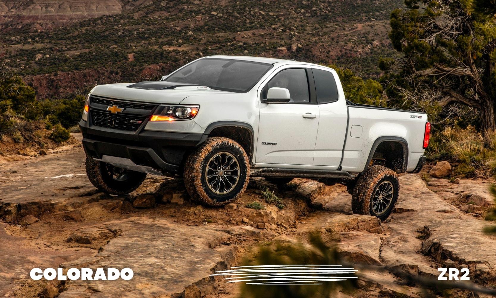 Best%20Used%20Chevy%20Colorado%20ZR2%20Trucks%20-%20Octane%20GMC%20of%20Santa%20Fe.jpg a white used Chevy Colorado ZR2 truck off-road driving over some rocks with muddy tires