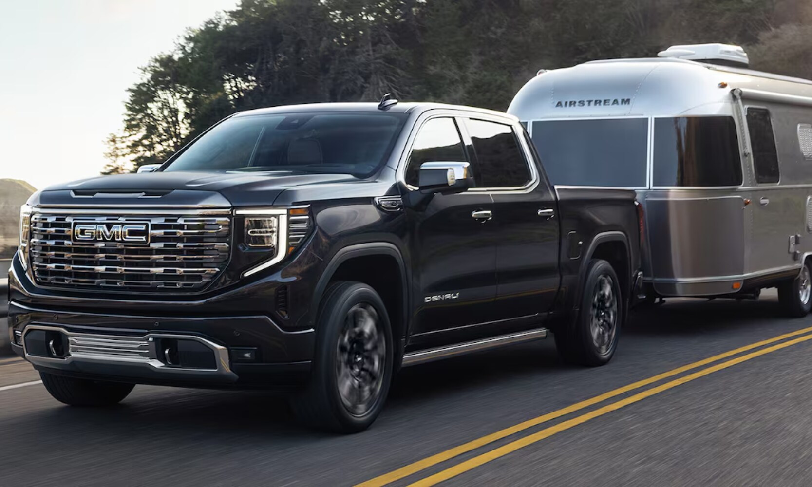 2025%20GMC%20Sierra%201500%20vs.%202025%20RAM%201500%20-%202025%20GMC%20Sierra%201500%20Towing%20Comparison-%20Octane%20GMC%20of%20Santa%20Fe.jpg Exterior front angle image of a black 2025 GMC Sierra 1500 towing a camping trailer on a highway