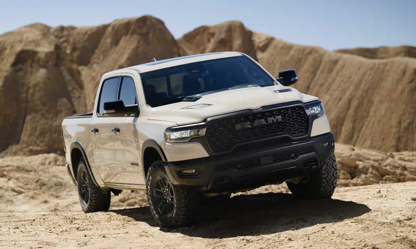 2025 GMC Sierra 1500 vs. 2025 RAM 1500 - 2025 RAM 1500 Rebel X - Octane GMC of Santa Fe.jpg Exterior front angle image of a white 2025 RAM 1500 Rebel X parked in a dirt landscape with mountains in the background