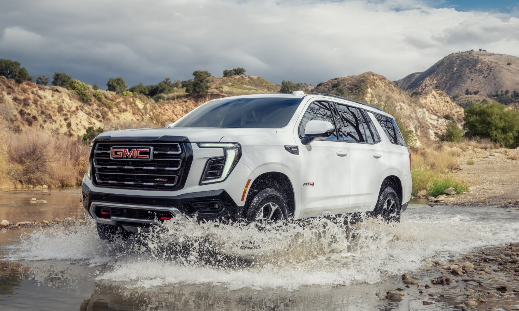 2025%20GMC%20Yukon%20vs.%202025%20Chevrolet%20Tahoe%20-%202025%20GMC%20Yukon%20AT4%20-%20Octane%20GMC%20of%20Santa%20Fe.jpg Exterior front image of a white 2025 GMC Yukon AT4 treading water in a mountainous landscape