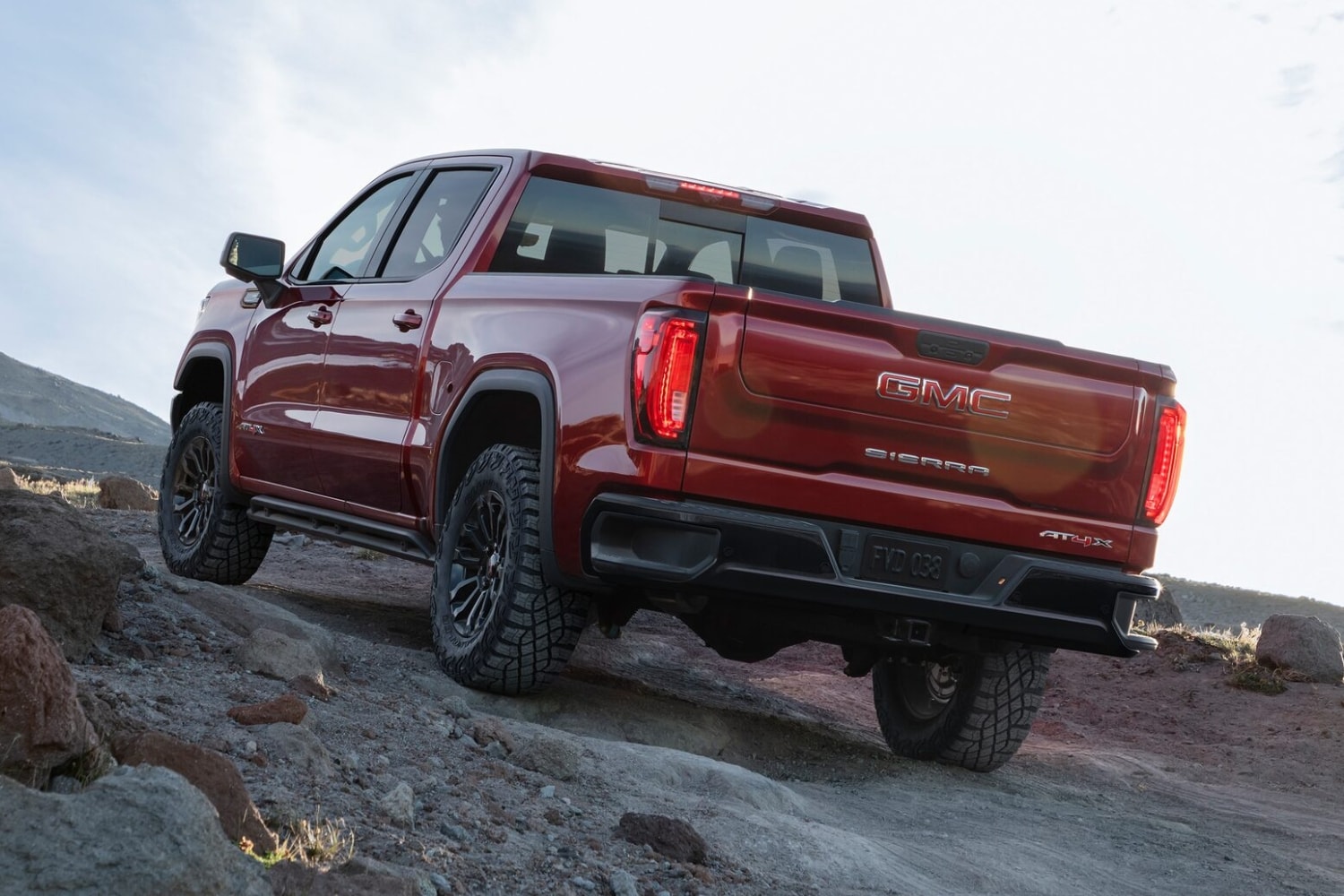 Rear exterior view of a volcanic red 2023 GMC Sierra 1500 AT4X driving up a steep off-road hill