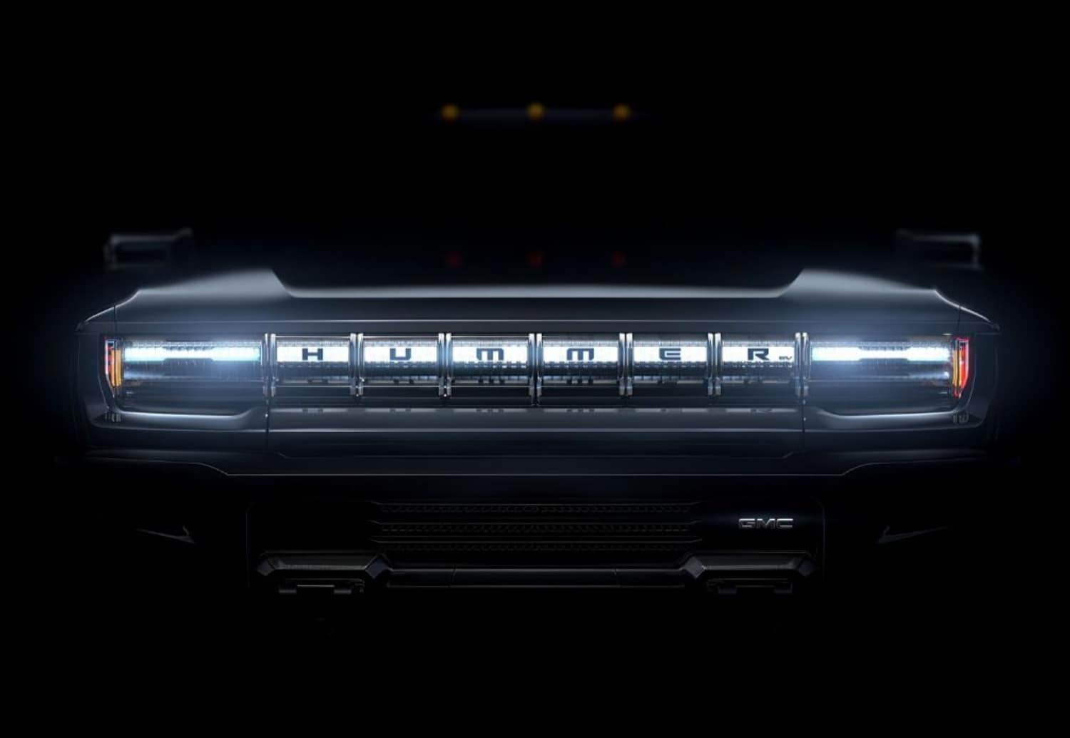 The front LED headlight bar on the 2024 GMC Hummer EV SUV glowing brightly in the dark