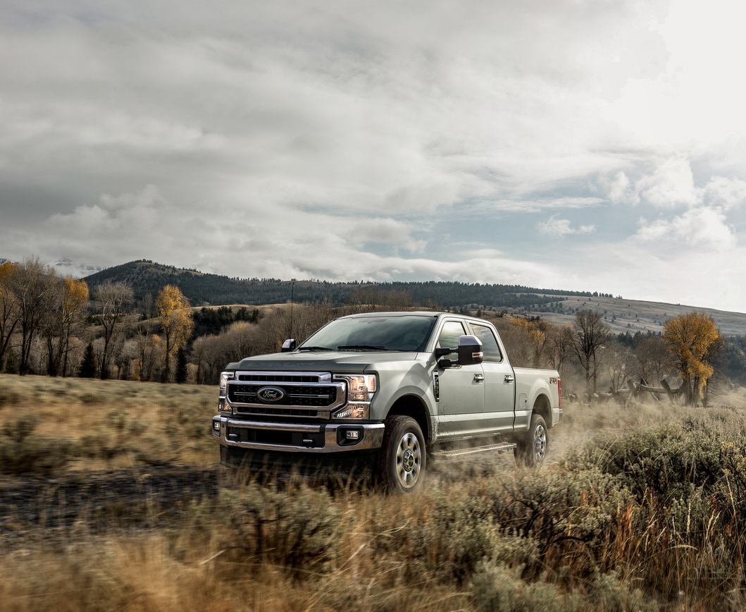 2022-Ford-F250-Larait-SuperCrew-Truck.png silver Ford F-250 truck parked in a grassy field under a cloudy sky