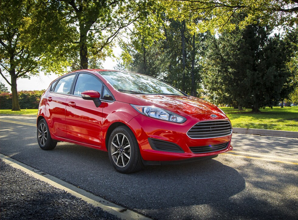 2016-Ford-Fiesta-SE-Hatchback-L01.png red Ford Fiesta driving by a green park