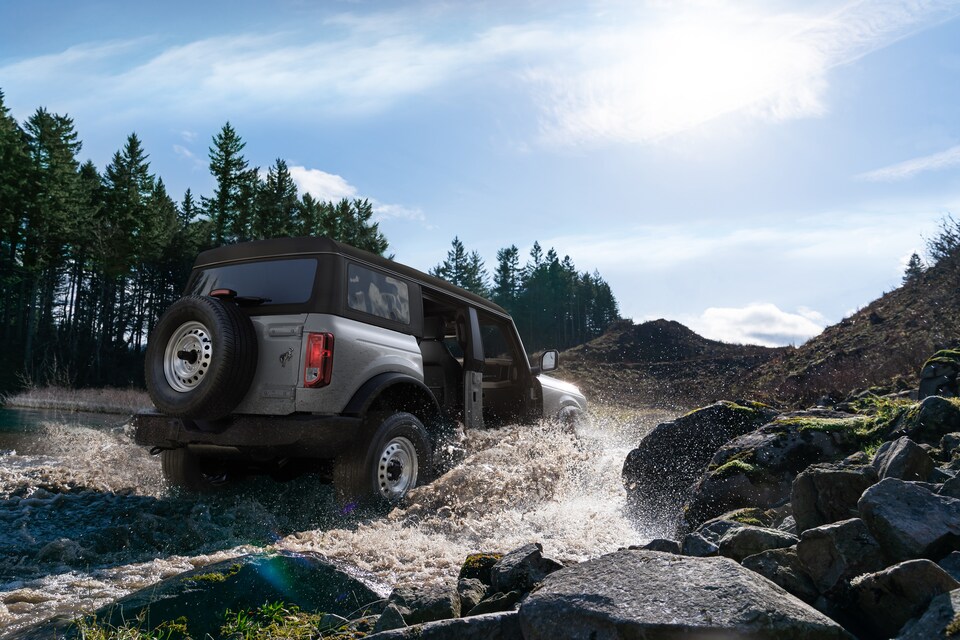 2021-Ford-Bronco-Base-4Door-SUV-L01.png silver Ford Bronco SUV wading through a river, doors removed