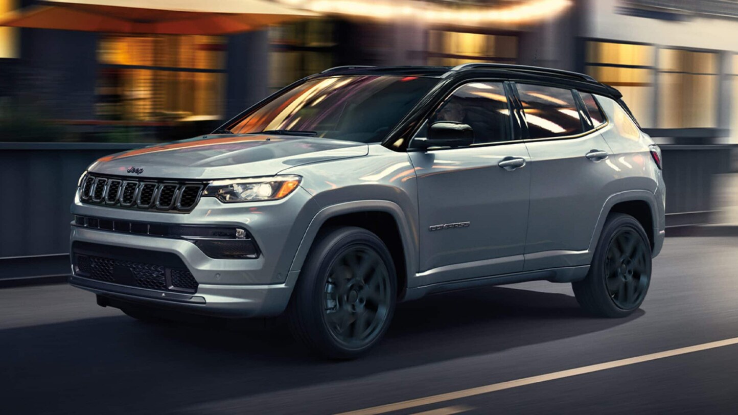 A silver Jeep Compass driving over a bridge in a city.