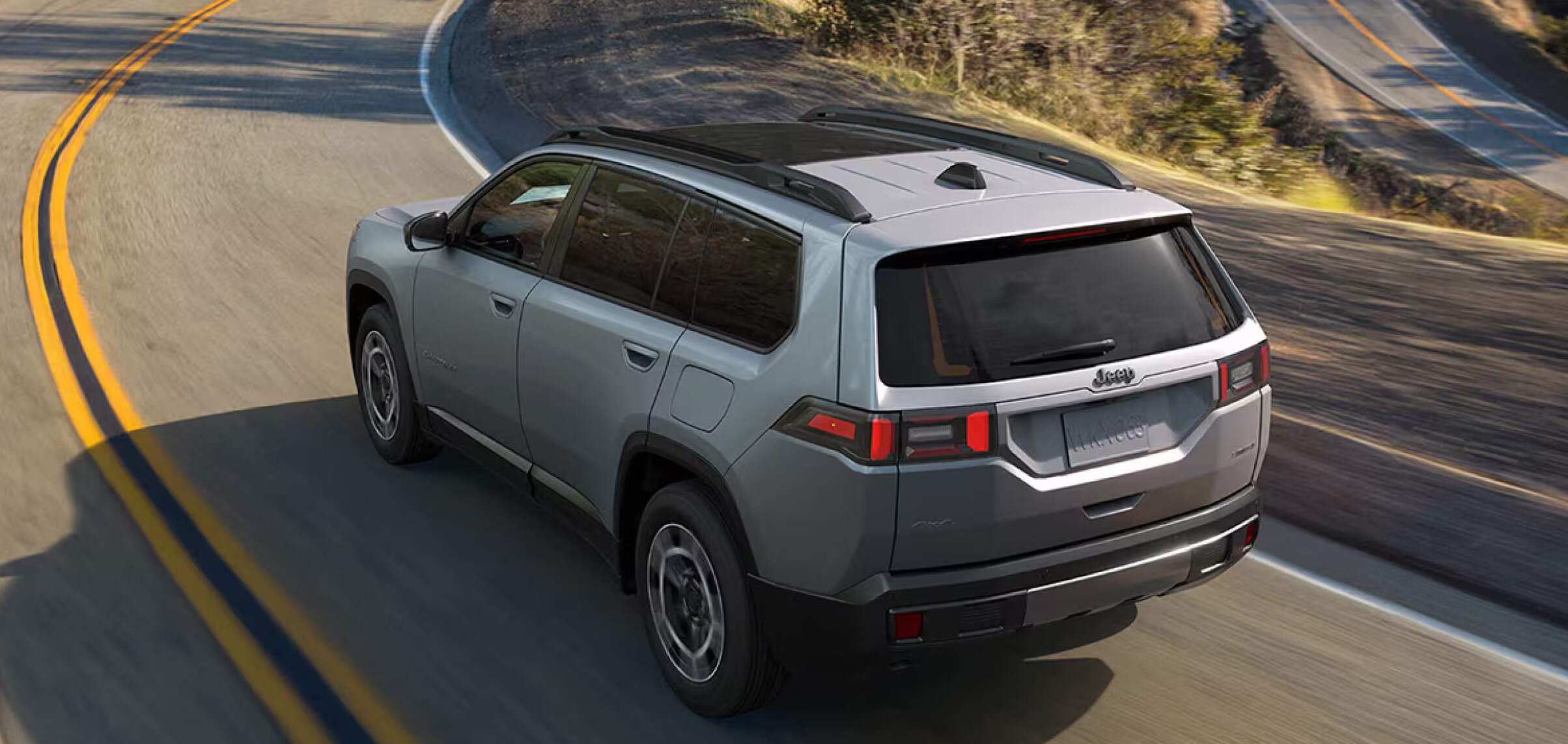 A gray 2026 Jeep Cherokee driving downhill on a winding road.