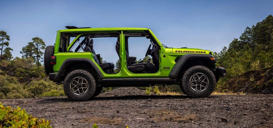 A lime green Jeep Wrangler with the doors off in profile in a dirt clearing.