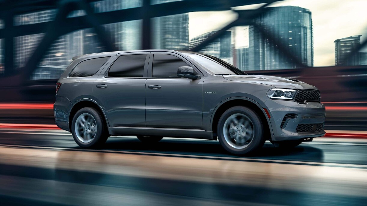 A gray Dodge Durango driving over a bridge in a city.