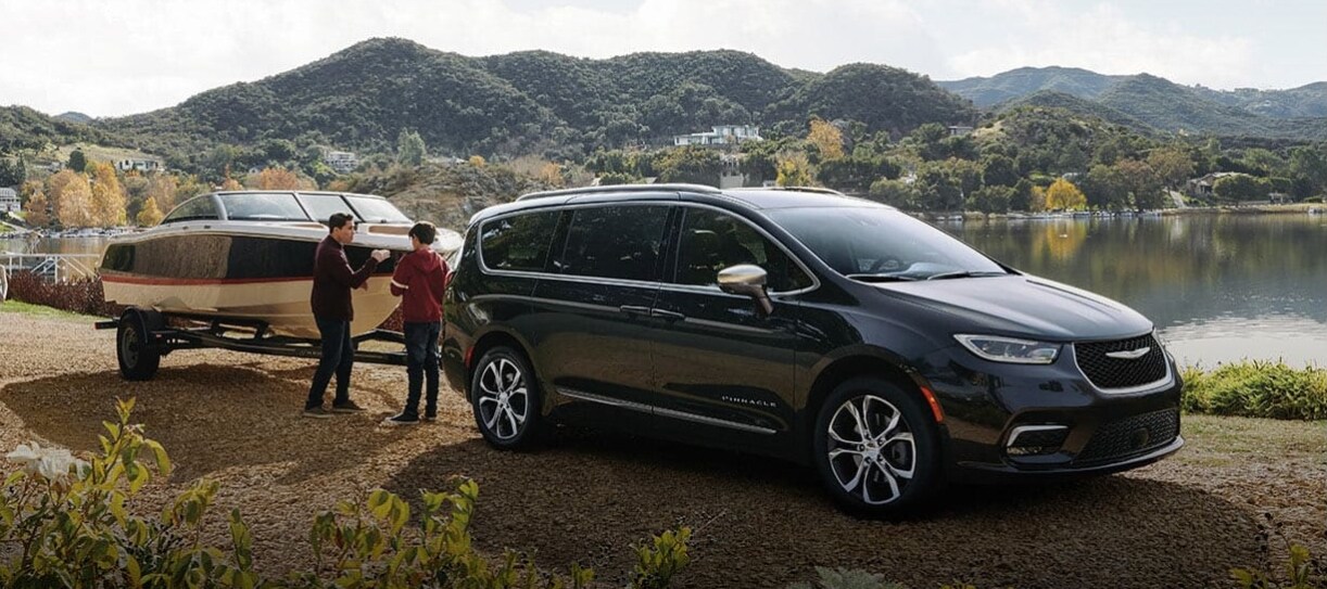 A black 2026 Chrysler Pacifica parked by a lake and towing a boat. A black 2026 Chrysler Pacifica parked by a lake and towing a boat.
