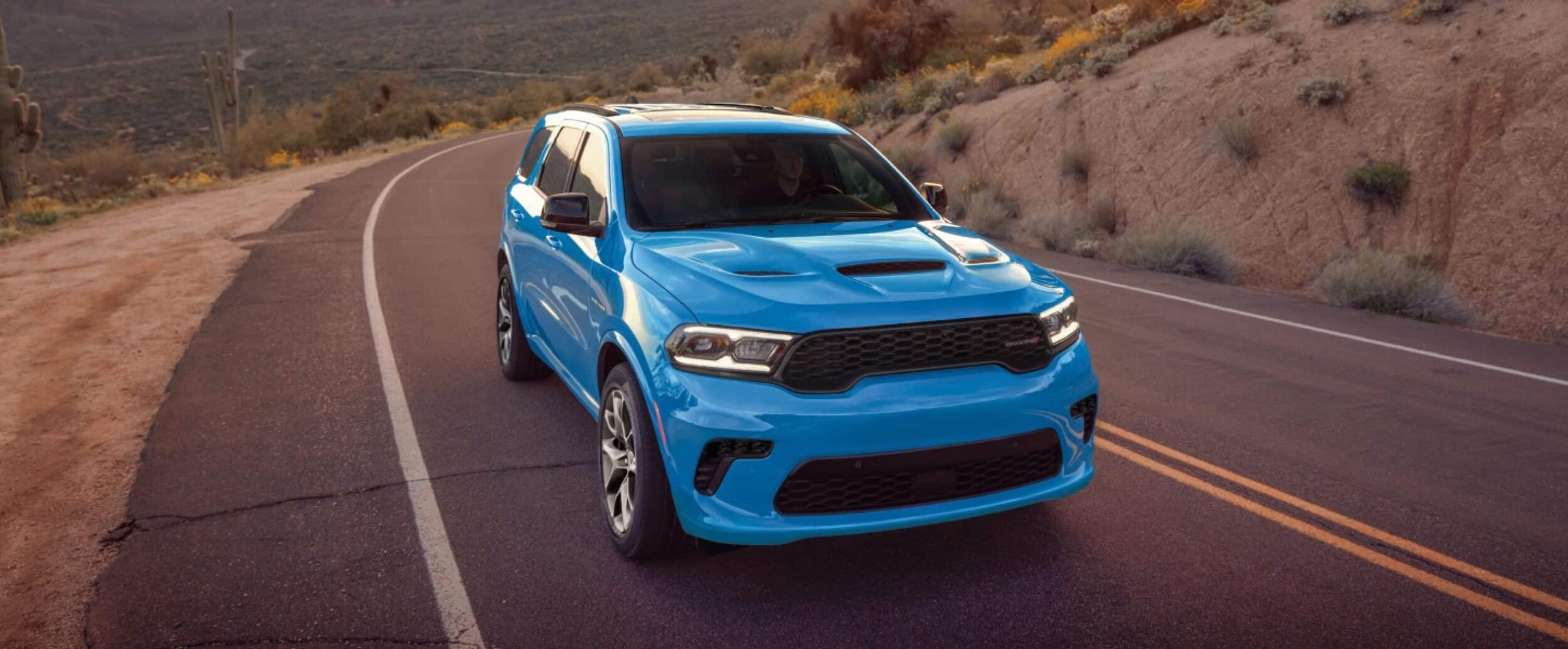 A light blue Dodge Durango driving down the road in a desert.