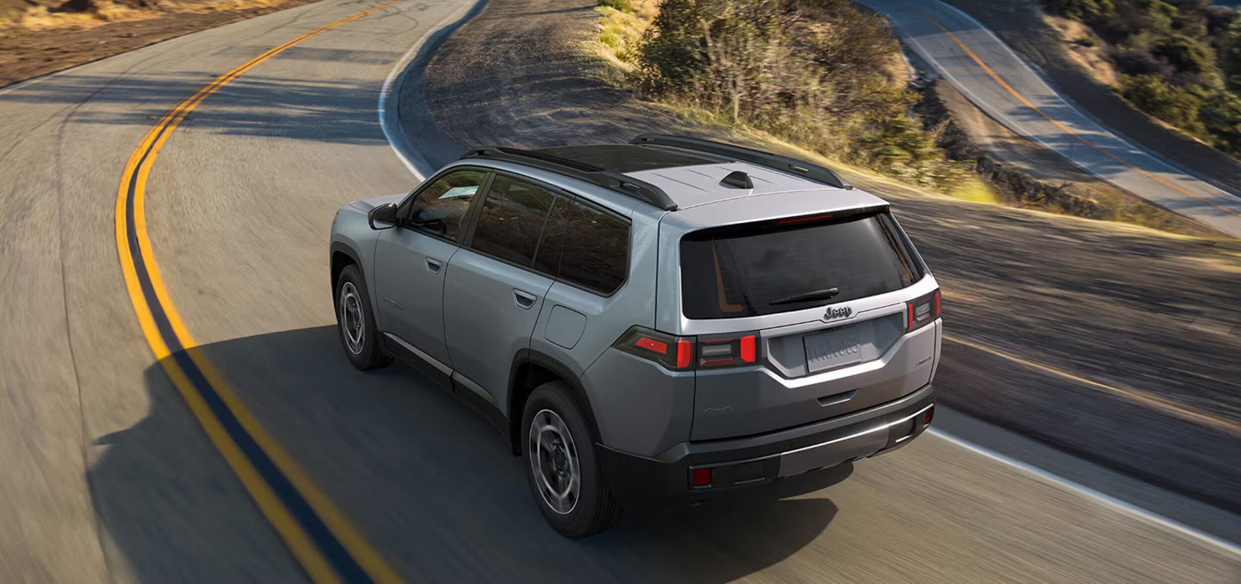 A gray 2026 Jeep Cherokee driving downhill on a winding road. A gray 2026 Jeep Cherokee driving downhill on a winding road.