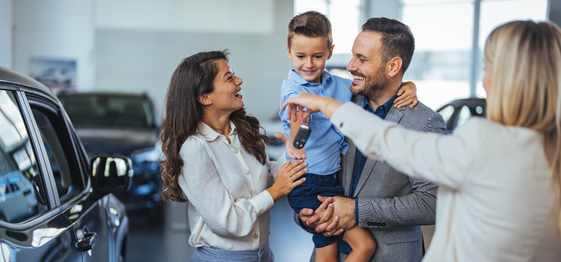 A family receiving the keys to their new car from a woman salesperson at a car dealership. A family receiving the keys to their new car from a woman salesperson at a car dealership.