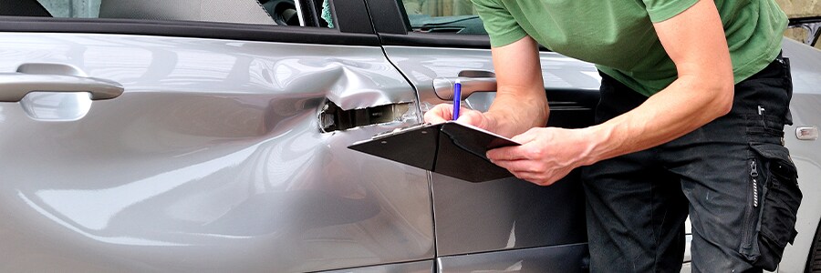 Dented Door of a Silver Car With a Man Holding aClipboard Looking at it