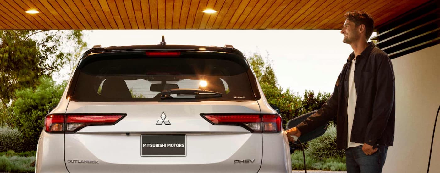 Mitsubishi Outlander PHEV for Sale - 2023 Mitsubishi Outlander PHEV - Charging Driveway.jpg A man plugging a white 2023 Mitsubishi Outlander PHEV into a home charger in his driveway.