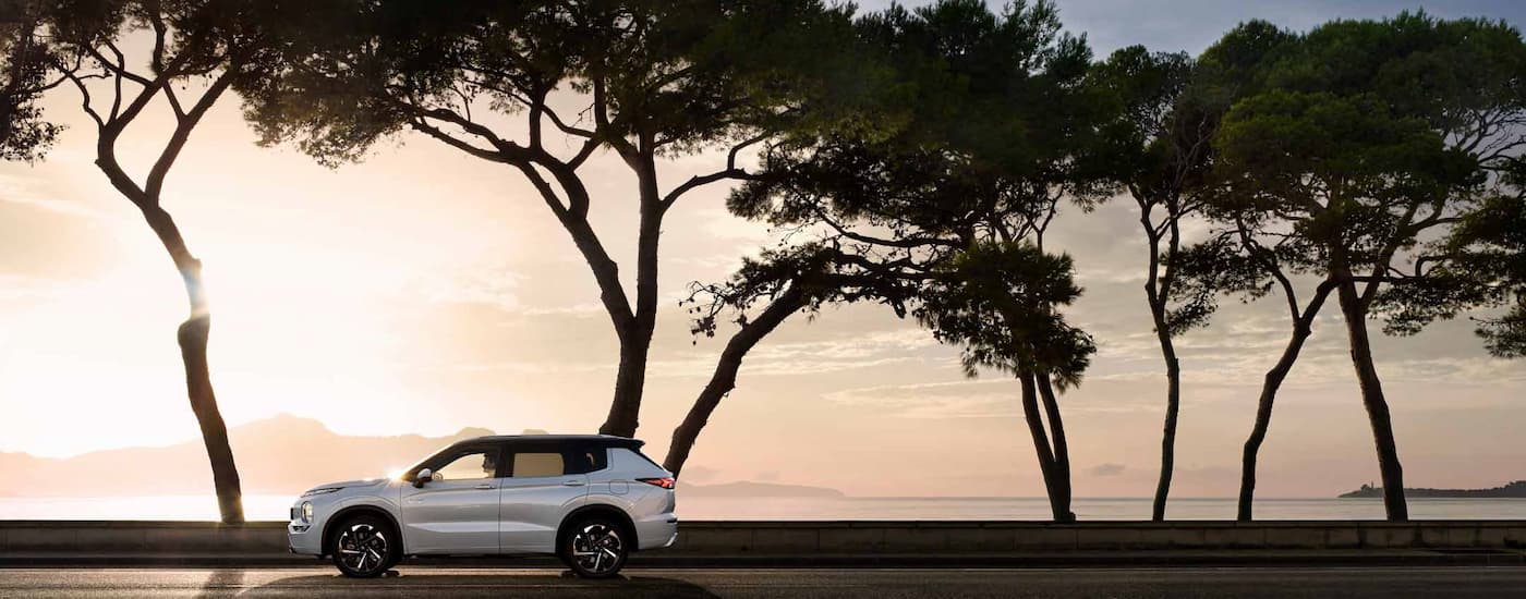 Mitsubishi Outlander PHEV for Sale - 2023 Mitsubishi Outlander PHEV - White Side Lake.jpg A white 2023 Mitsubishi Outlander PHEV parked next to tall trees at a lakeside.