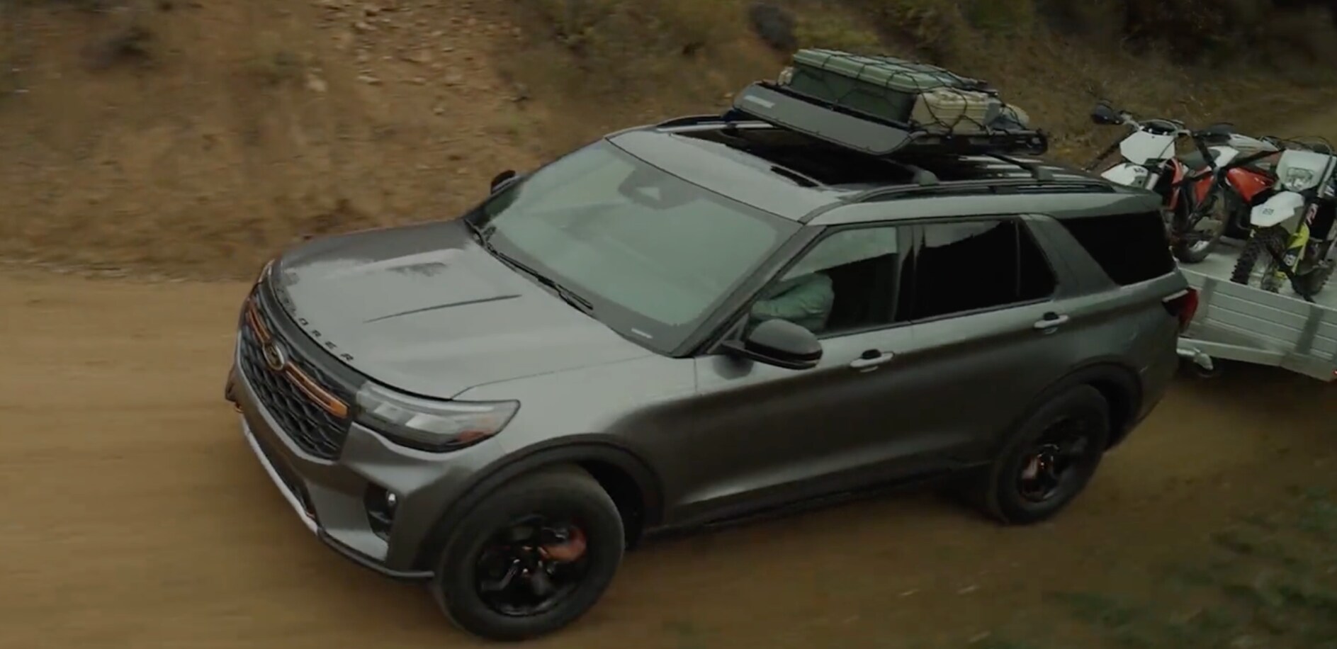 A gray Ford Explorer hauling gear while driving up a dirt road. A gray Ford Explorer hauling gear while driving up a dirt road.