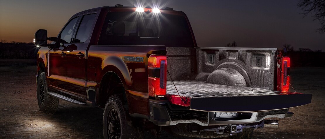 A rear image of a dark-colored Ford Super Duty at sunset, with rear lights on and the truck bed open